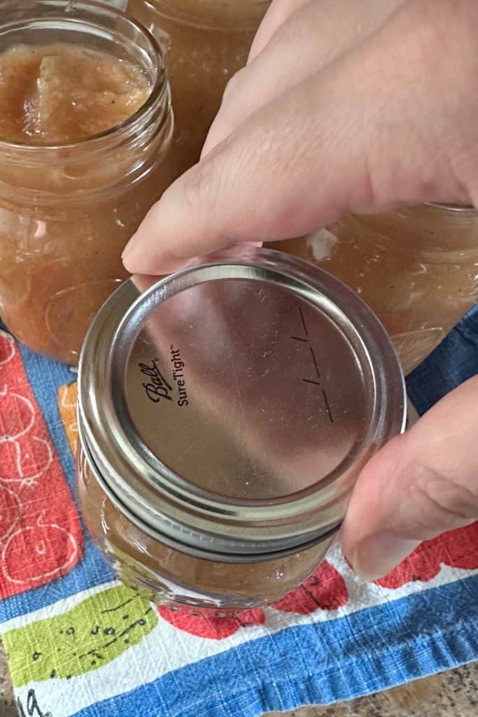 A person putting apple butter into a jar.