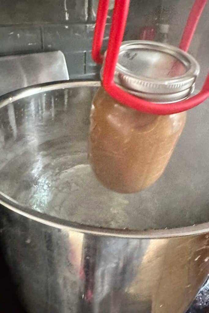 A jar of apple butter being put into a canning pot.