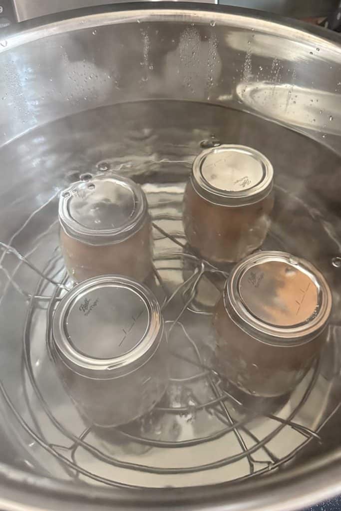 Four jars in a pot on top of a stove.
