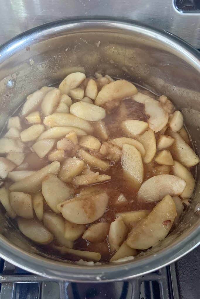 A pot with apples in it on top of a stove.