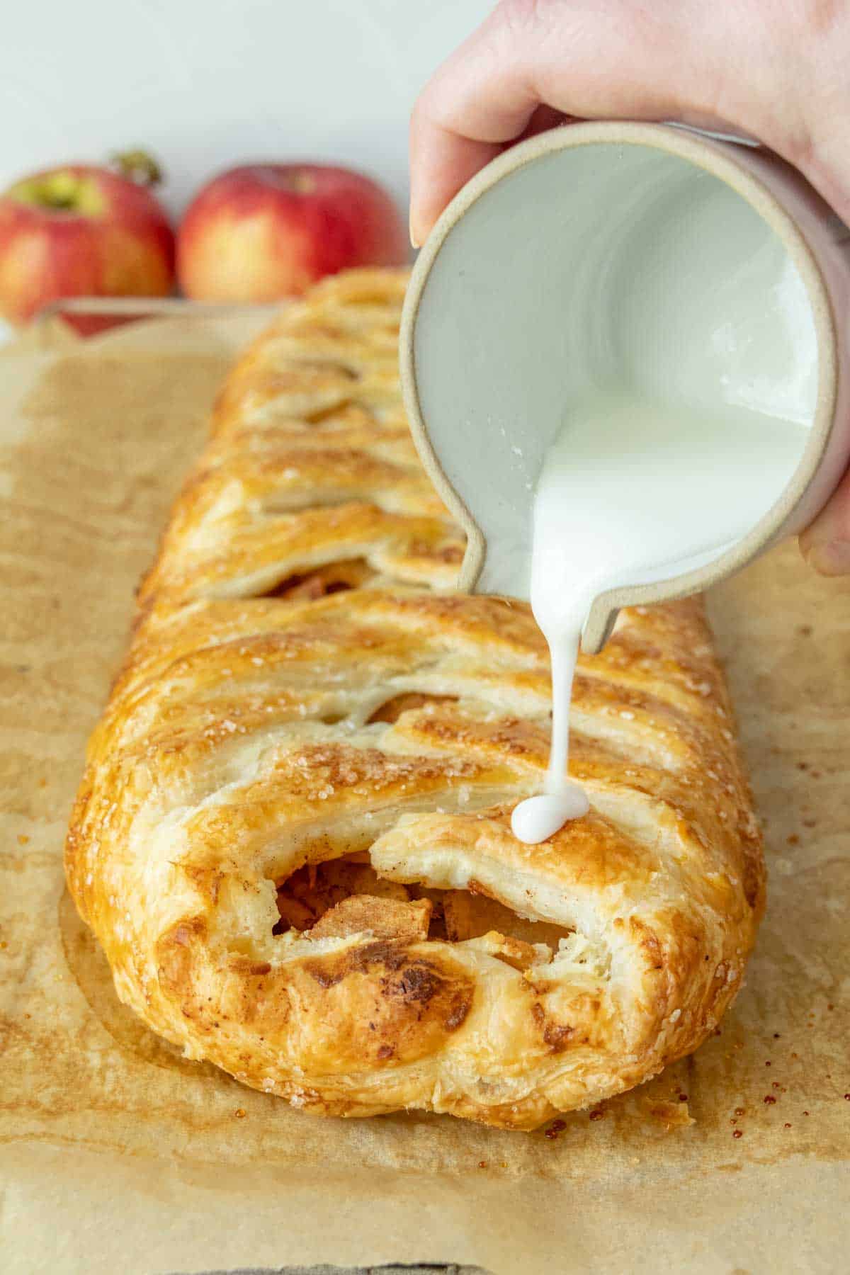 A person pouring icing onto an apple pastry.