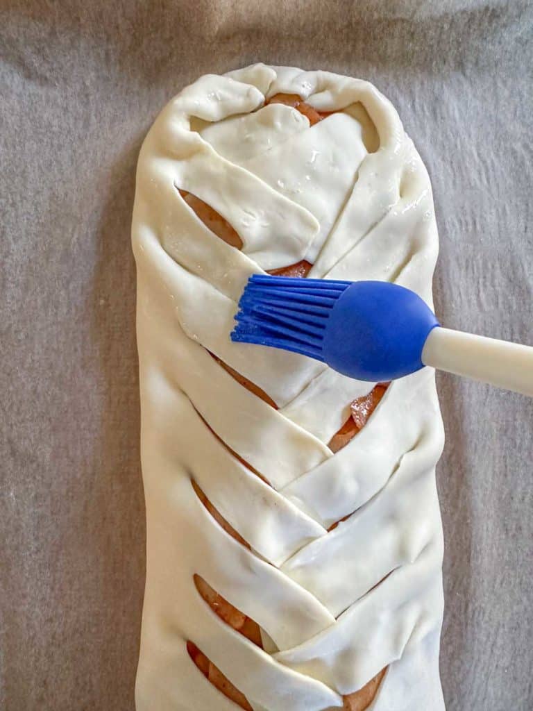 A braided bread being brushed with a blue brush.