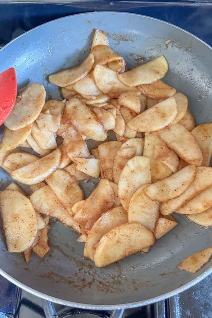 Apple slices in a frying pan with a red spatula.