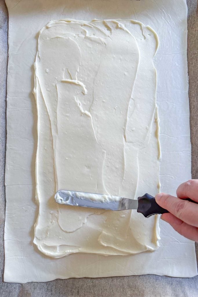 A person spreading cream cheese onto pastry dough.