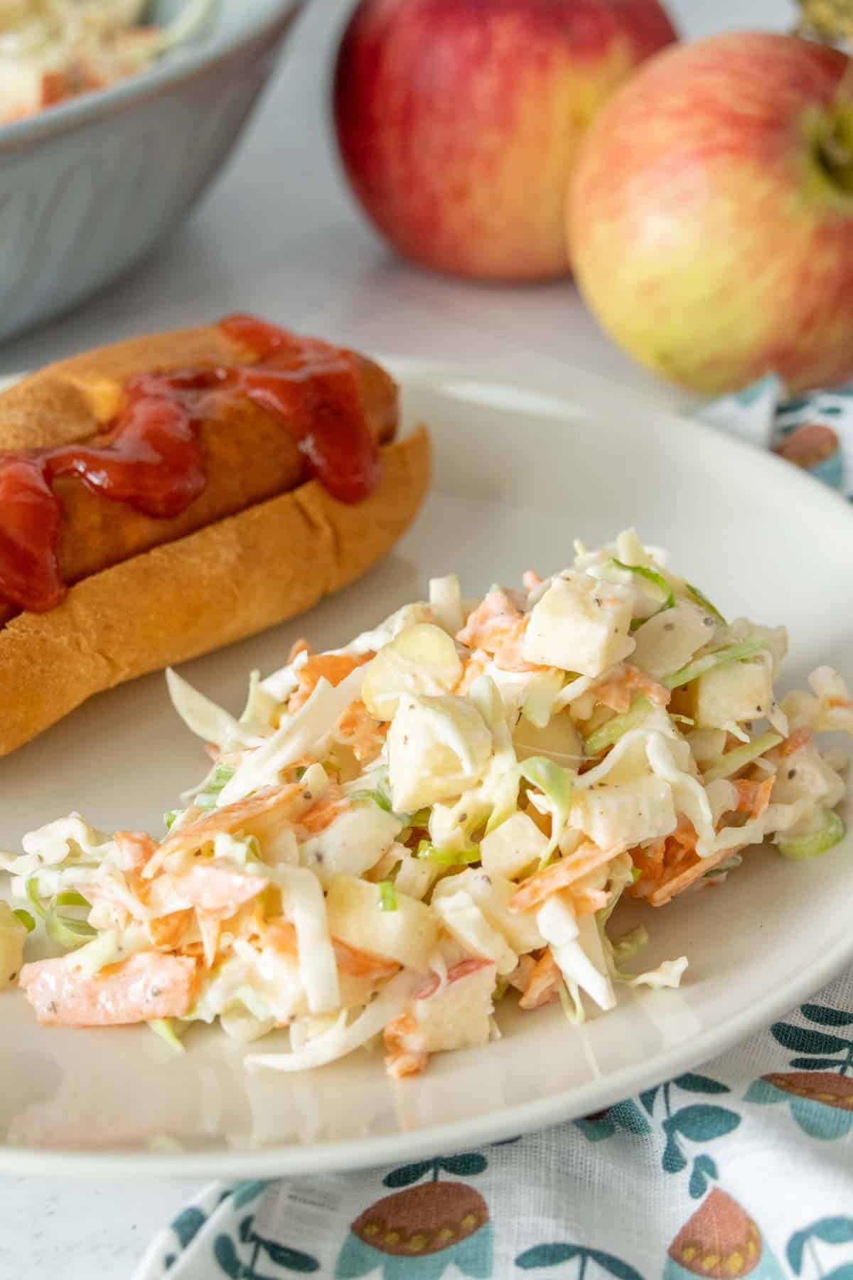 A hot dog with coleslaw and apples on a plate.