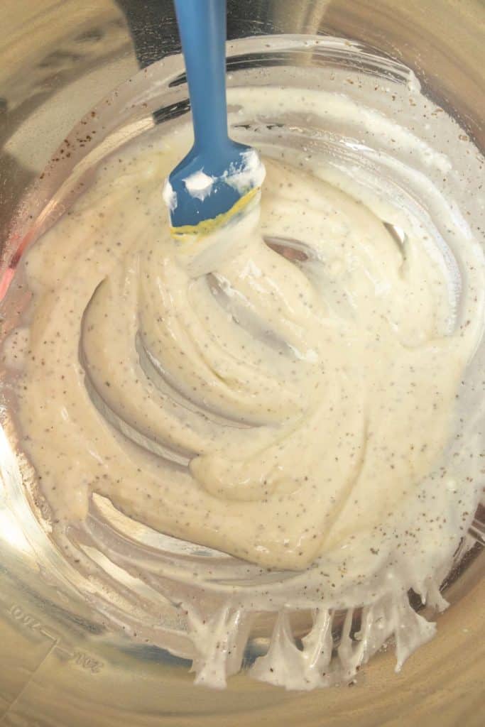 A blue spoon is being used to stir a bowl of coleslaw dressing.