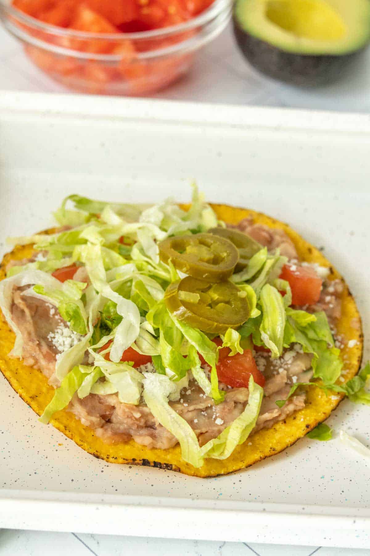 Tostada on a white plate with tomatoes and lettuce.