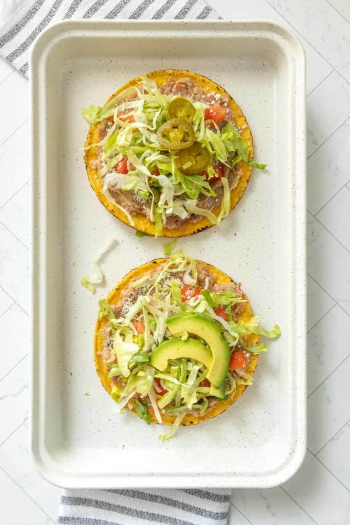 Two bean tostadas on a white plate with lettuce and tomatoes.