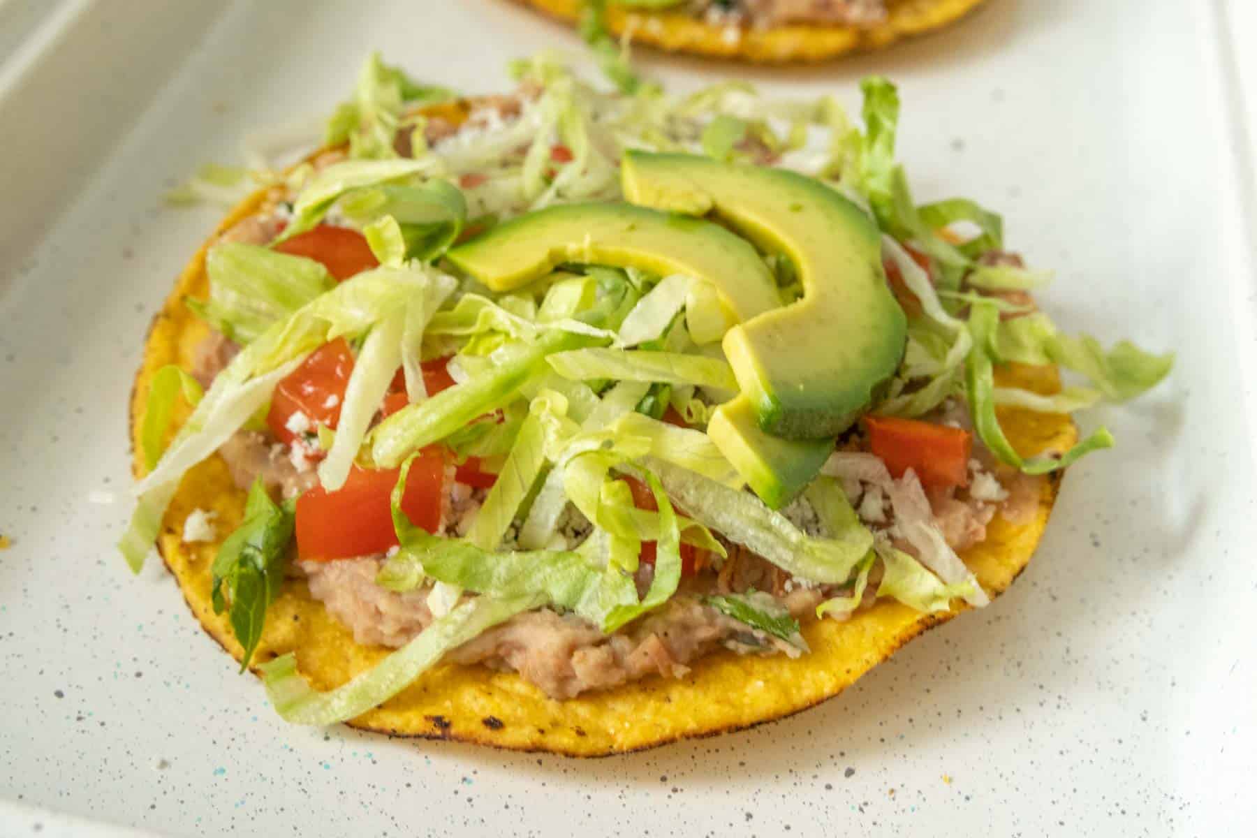 Bean tostadas topped with avocado, tomatoes and lettuce.