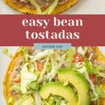 Two bean tostada shells topped with refried beans, shredded lettuce, avocado slices, diced tomatoes, cheese, and jalapeño—arranged on a white plate. Text overlay reads "easy bean tostadas.