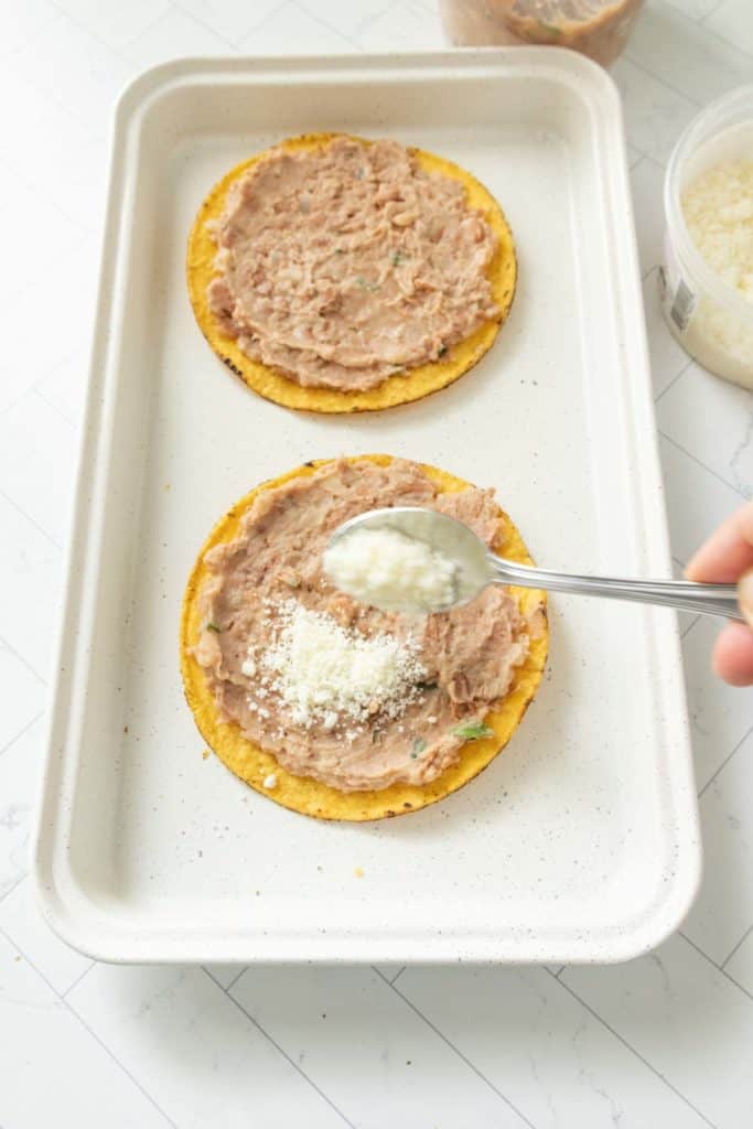 A person putting cheese on a tostada.