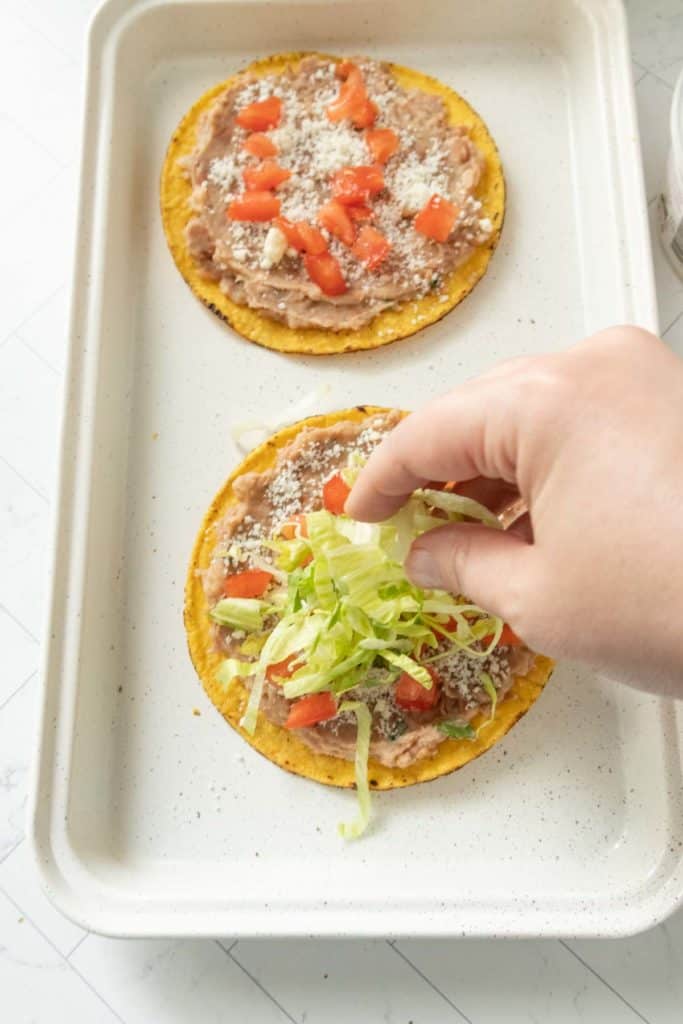 A person is putting toppings on a tostada.