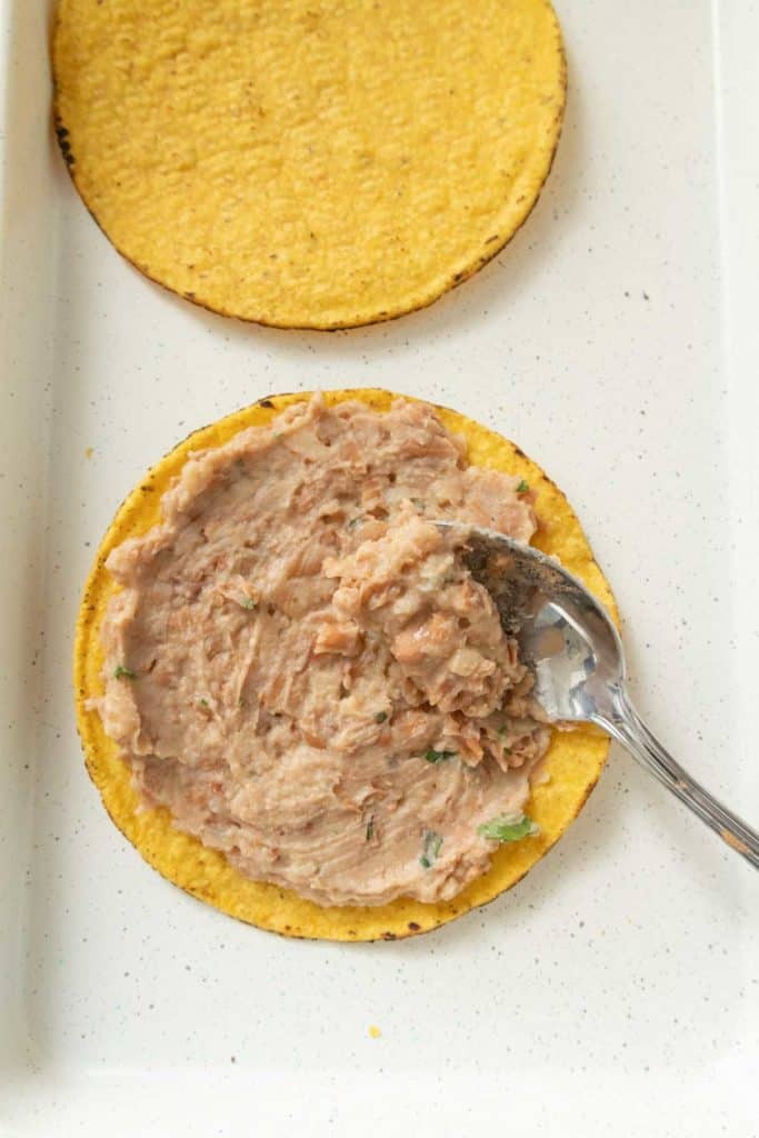Spreading refried beans on a tostada.