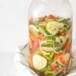 Cucumber pickles in a jar on a white cloth.