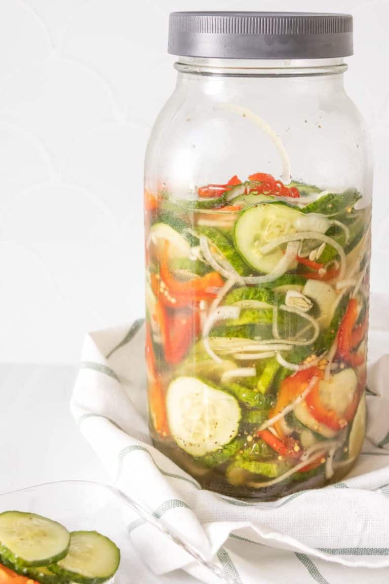 Cucumber pickles in a jar on a white cloth.