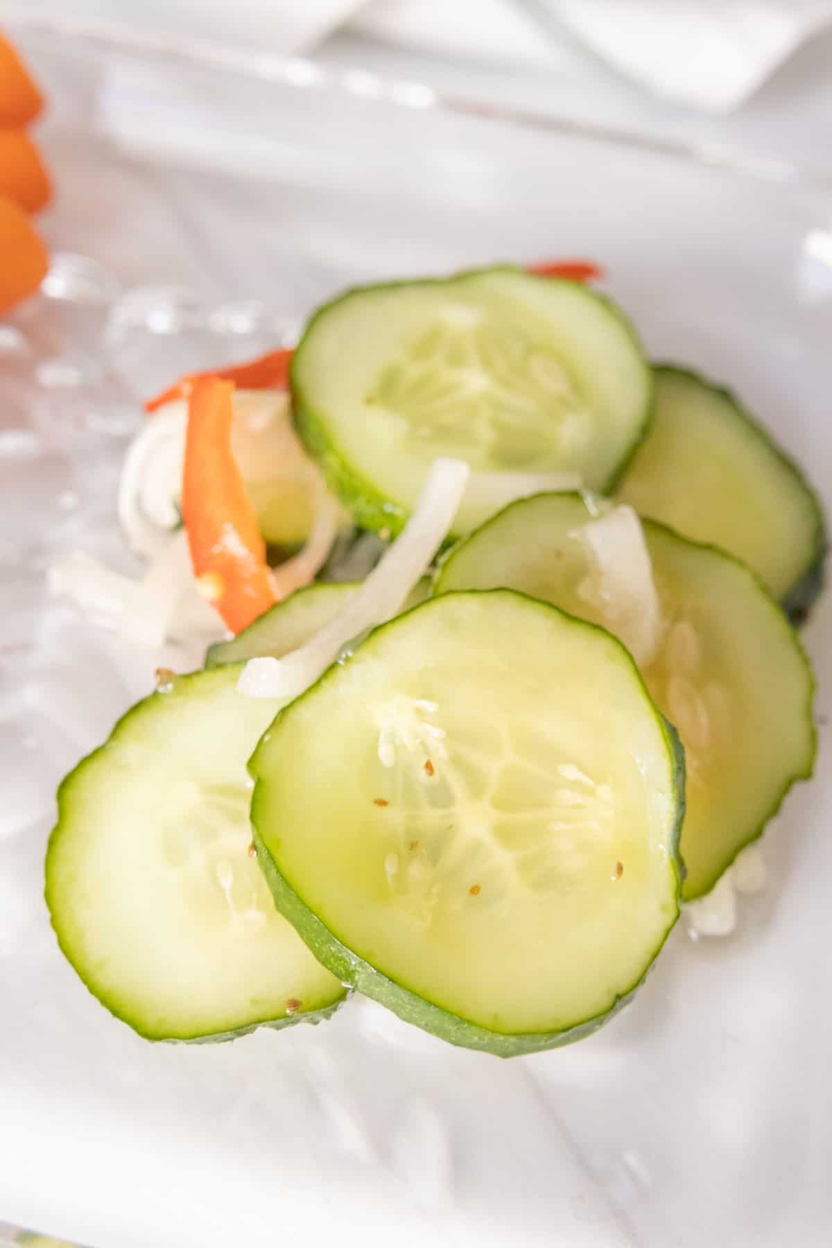 Sliced cucumber pickles and carrots on a white plate.