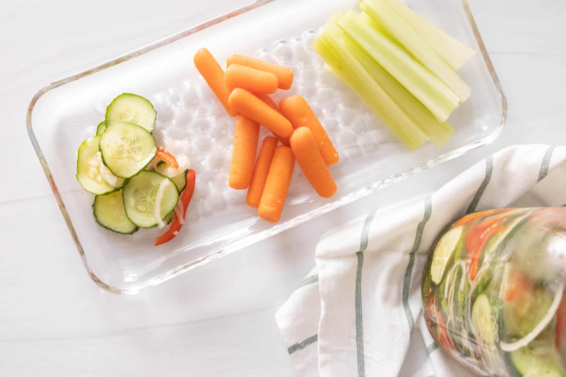 Cucumber pickles, carrots and celery on a glass plate.