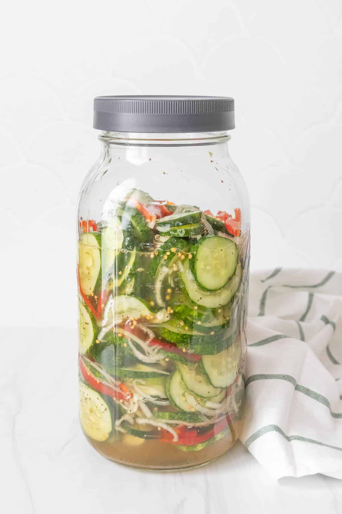 A jar with cucumbers and vegetables in it.