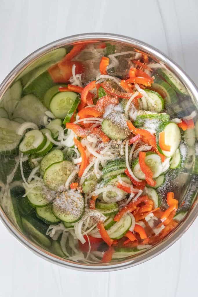 A bowl filled with cucumbers, peppers, and onions covered in spices.