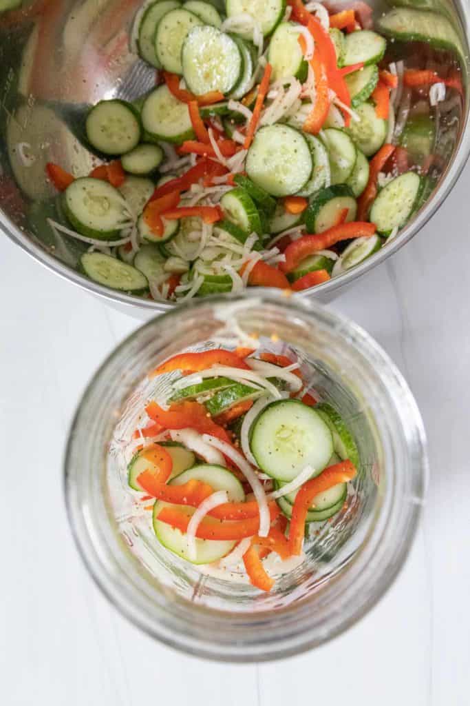 A jar with cucumbers, onions, and peppers in it.