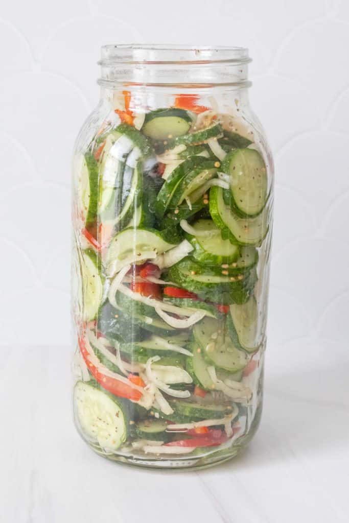 A jar filled with cucumbers, onions, and peppers.