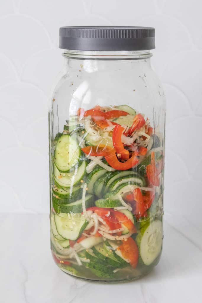 A jar filled with cucumbers, onions, and peppers.