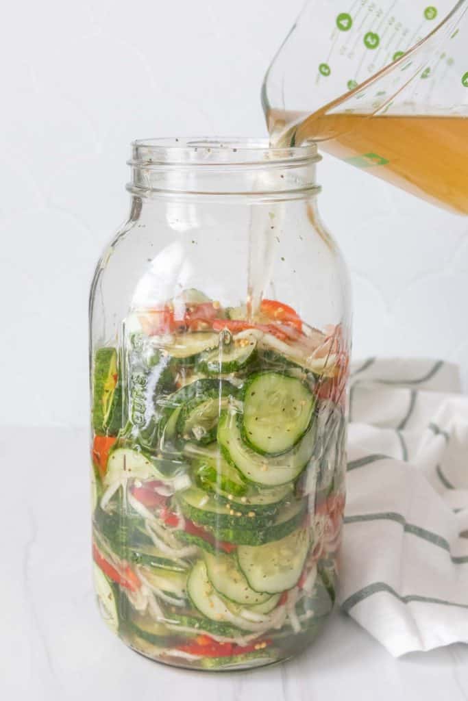 Cucumber pickles in a jar with liquid being poured into it.