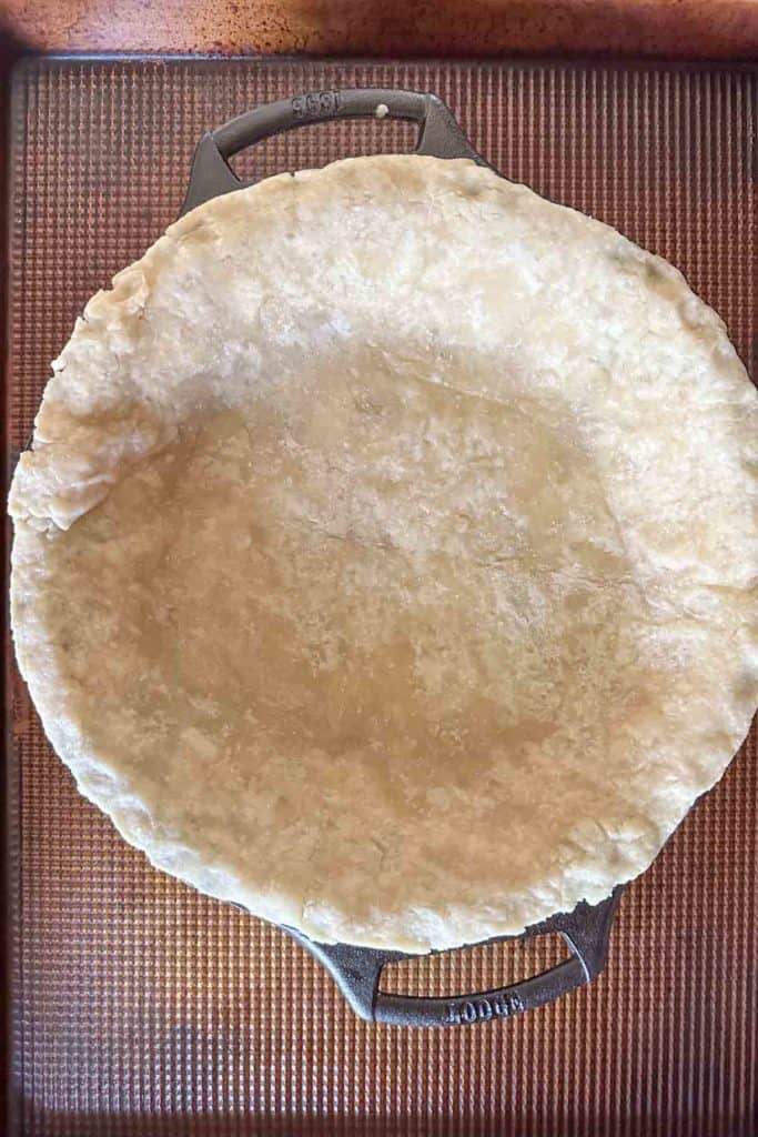 A pie crust in a metal pan on top of a baking sheet.
