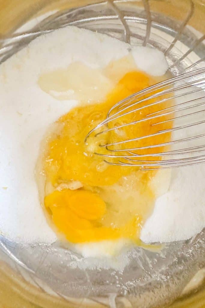 A whisk is being used to mix eggs with sugar in a bowl.