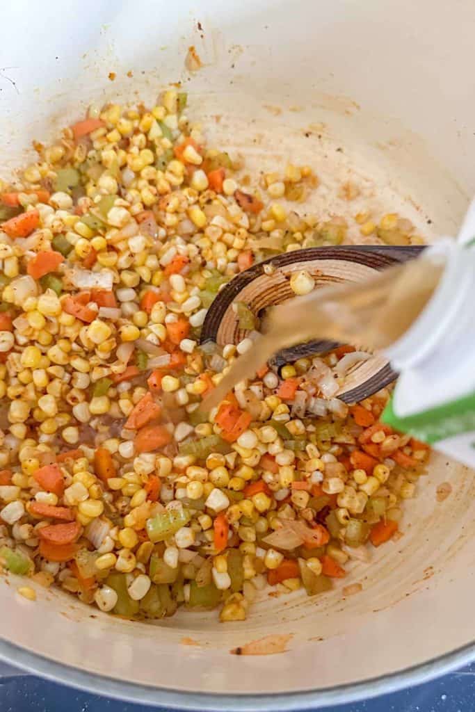Adding vegetable broth to vegetables for corn soup.