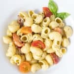 White bowl of creamy pesto pasta with cherry tomatoes.