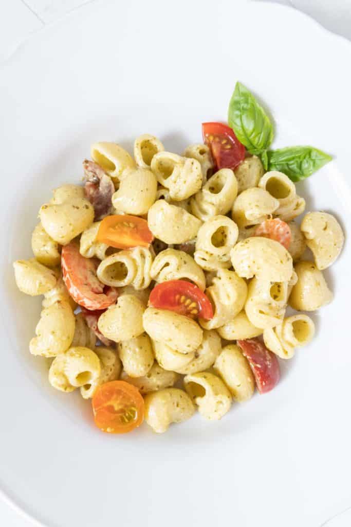 White bowl of creamy pesto pasta with cherry tomatoes.