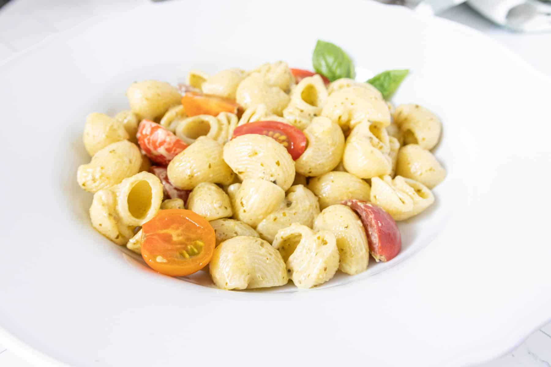 Low bowl of creamy pesto pasta and halved cherry tomatoes.