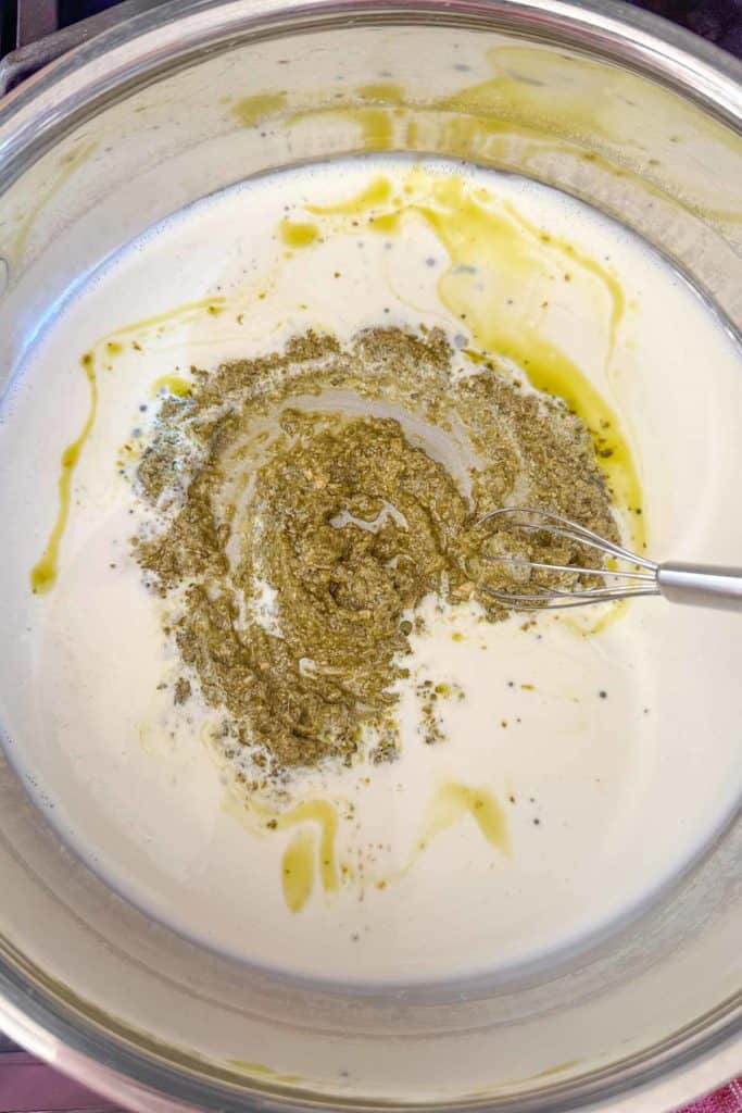 Whisking together pesto and cream in a skillet.