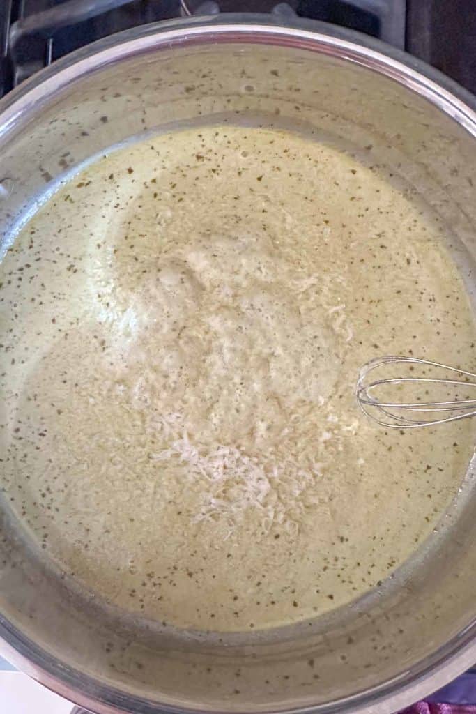 Whisking parmesan cheese into creamy pesto sauce in a saucepan.