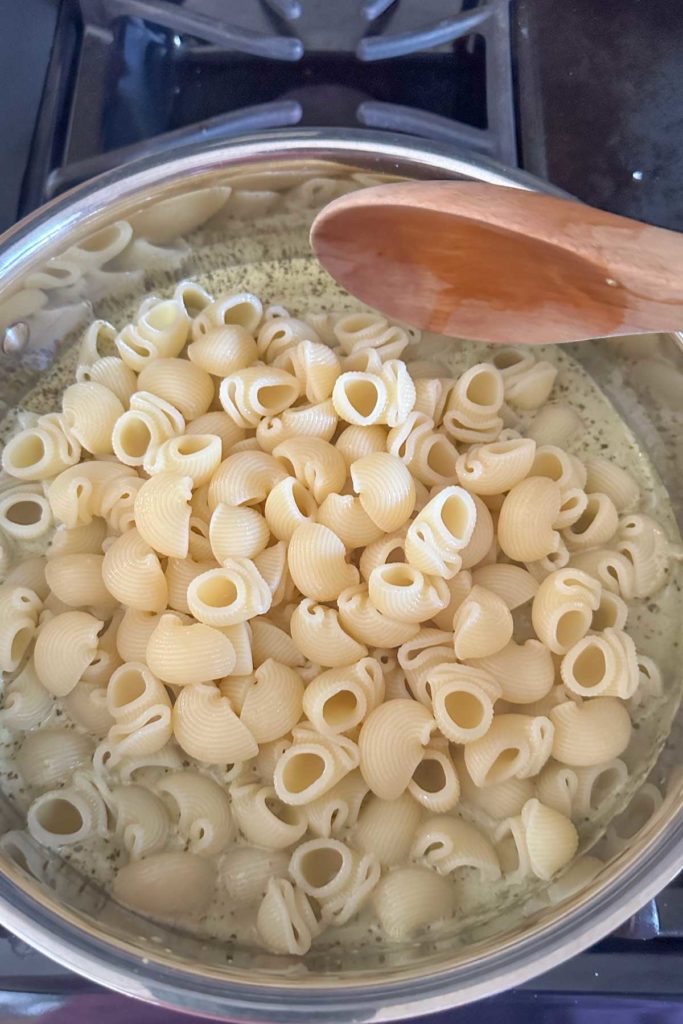 Stirring pasta into creamy pesto sauce in a skillet.