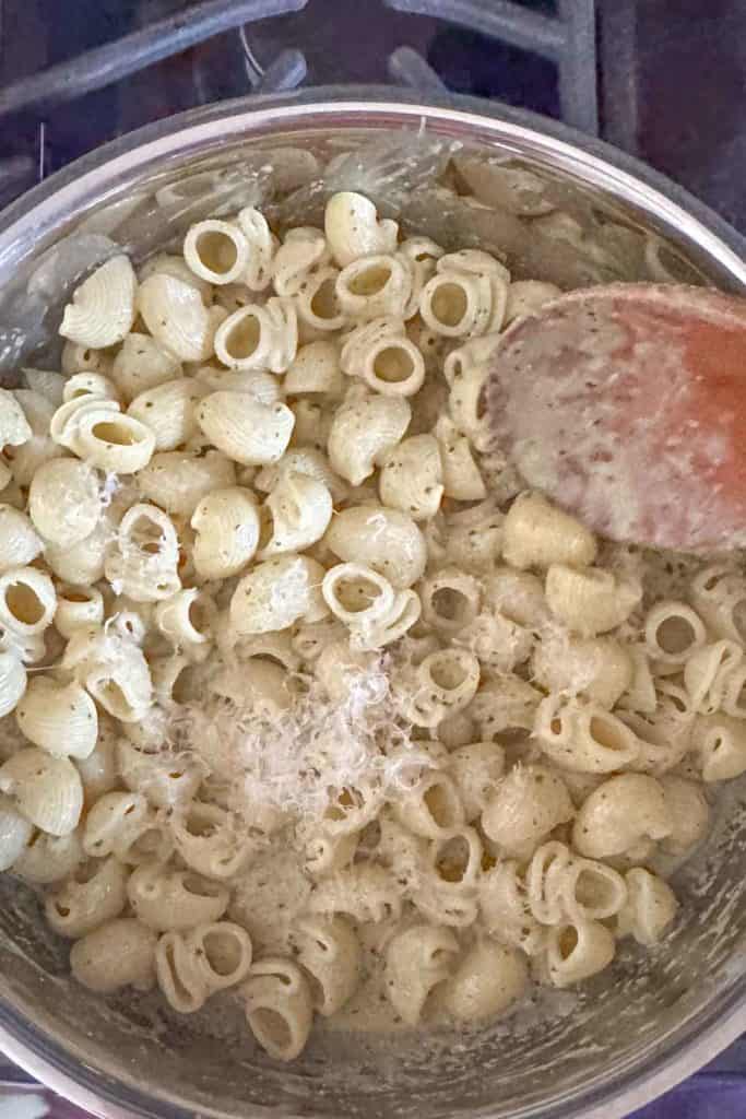 Stirring cheese into pesto pasta.