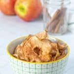 Apple chips in a bowl with cinnamon sticks.
