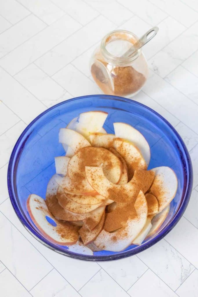 Apple slices in a blue bowl with cinnamon.