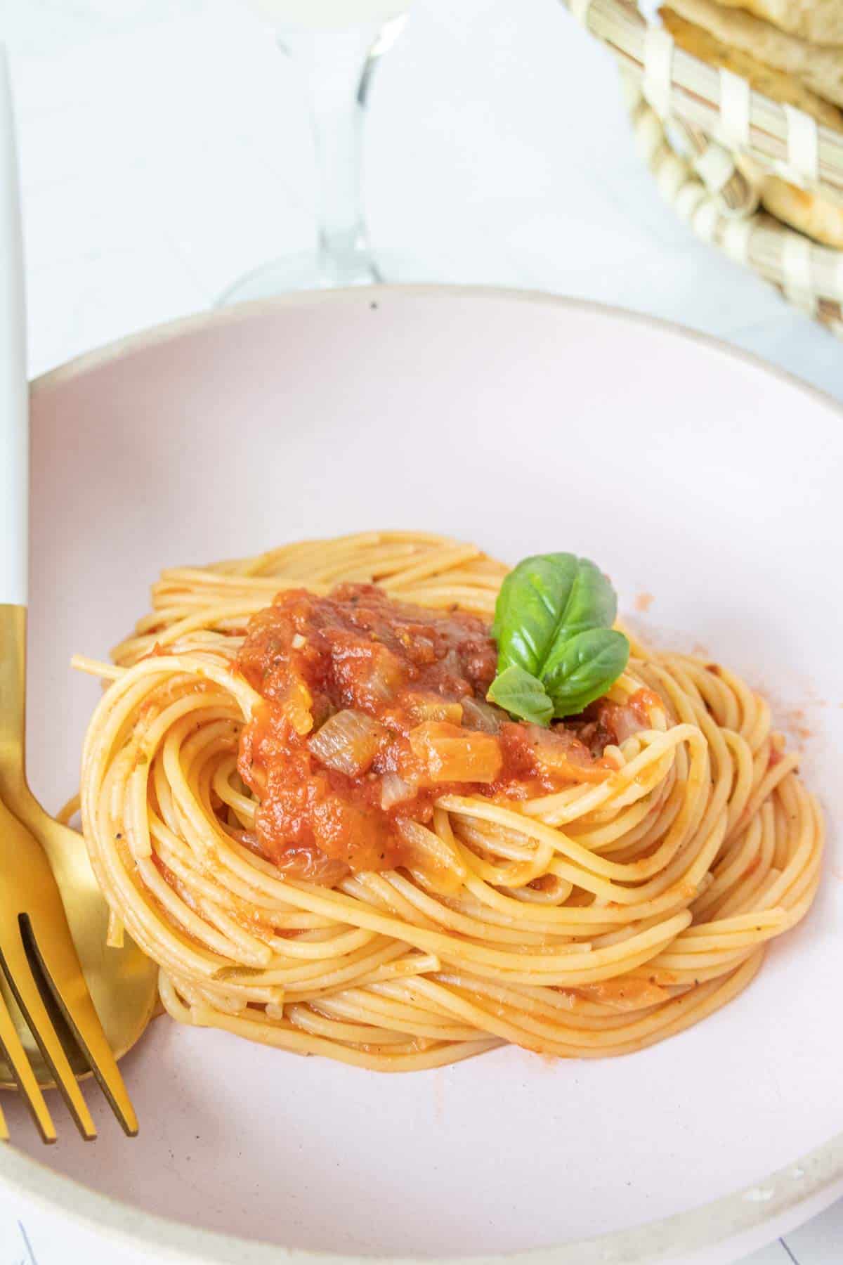 Spaghetti with tomato sauce on a pink plate with a fork.