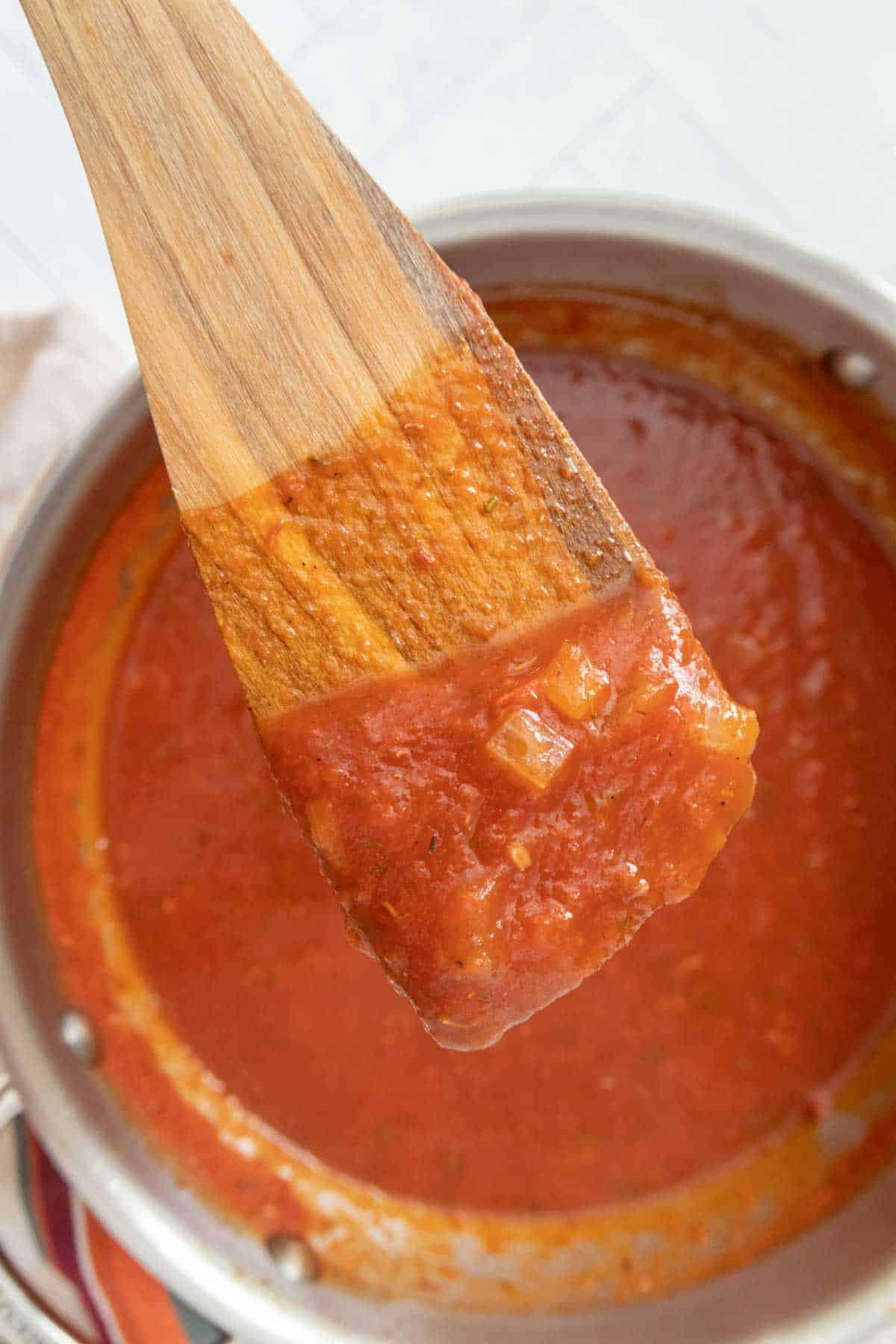 A wooden spoon is being used to stir a pot of tomato sauce.