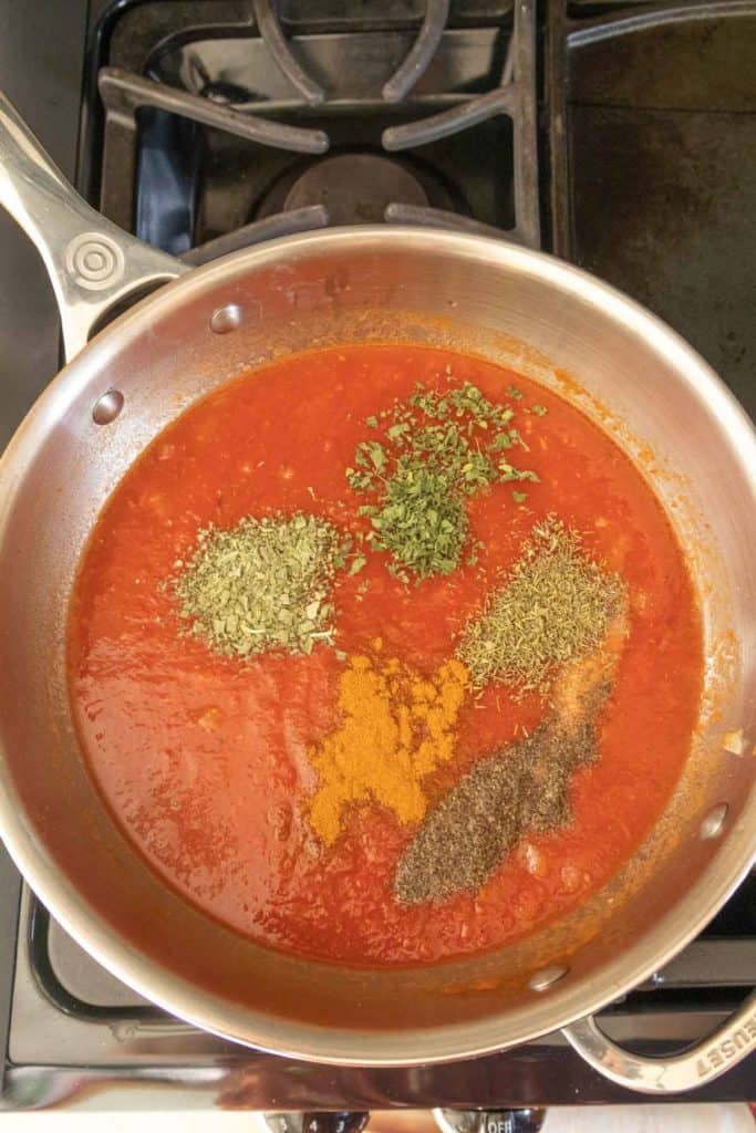 A pan full of tomato sauce and spices on a stove.