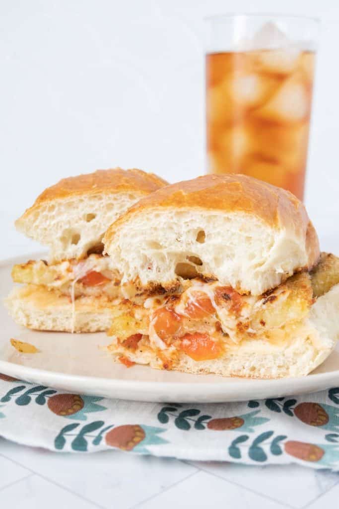 Eggplant parmesan sandwich on a cream plate with a glass of iced tea.