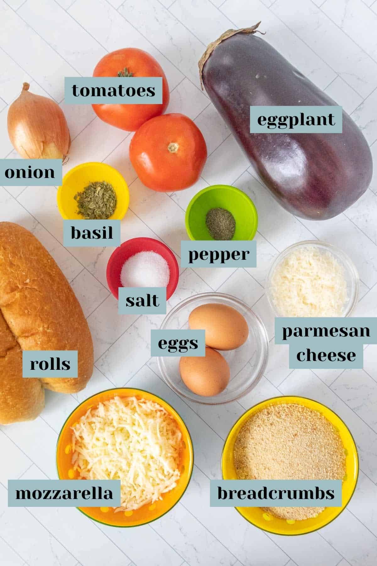 Ingredients for eggplant parmesan sandwich on a tile surface with labels.