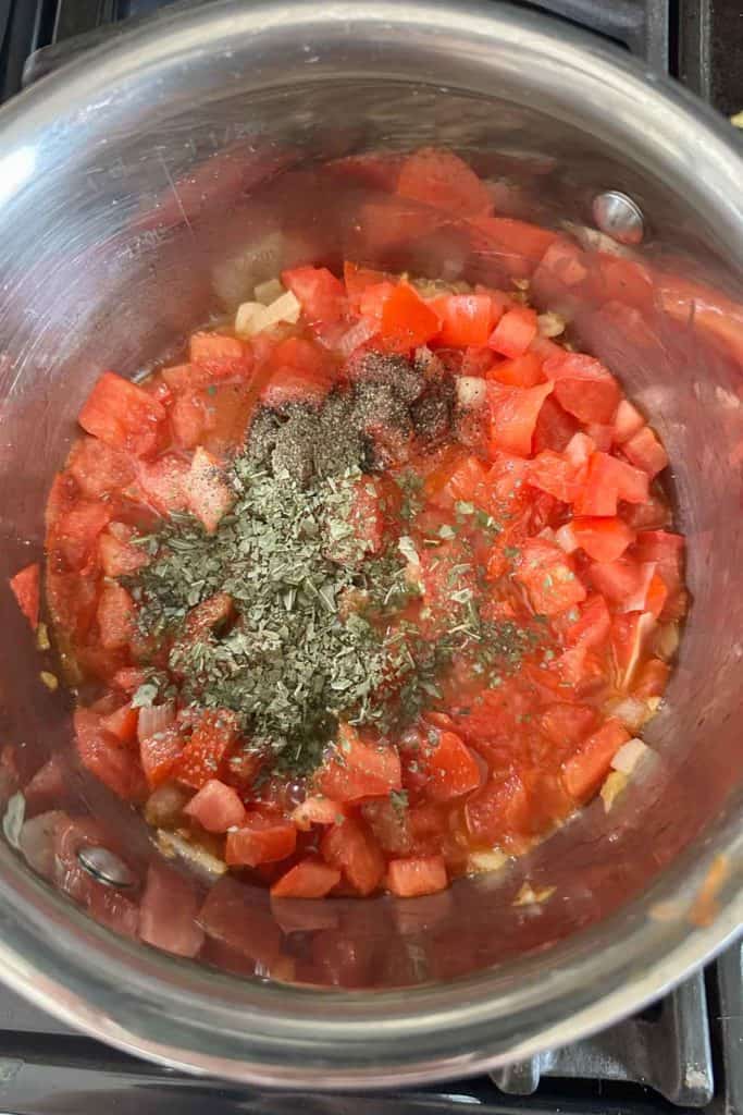 Spices added to tomatoes and onions in a saucepan.