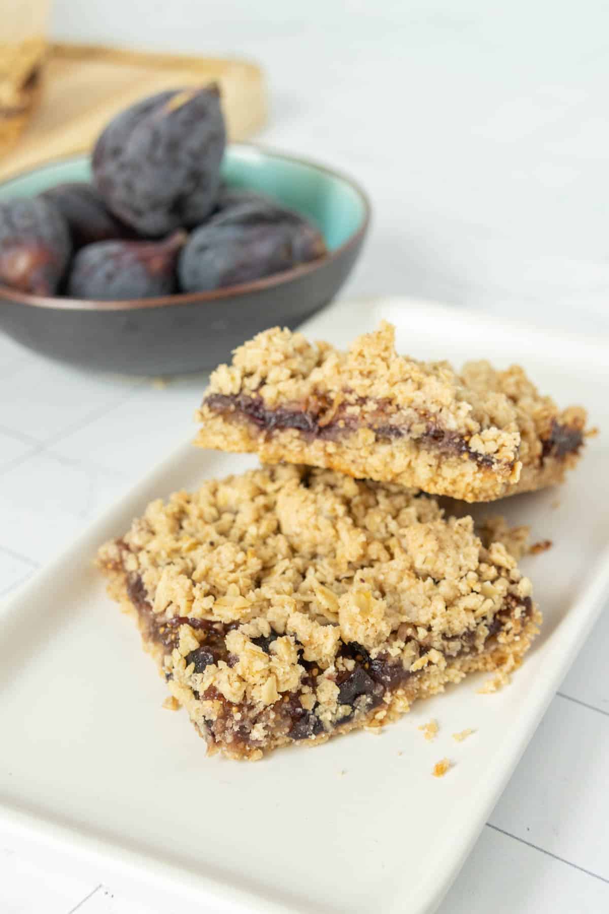 Fig bars on a white plate with a bowl of figs.