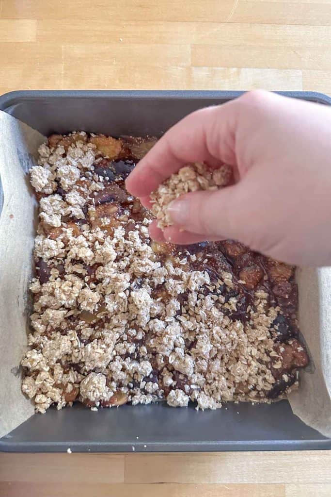 A person sprinkling crumble into a pan.