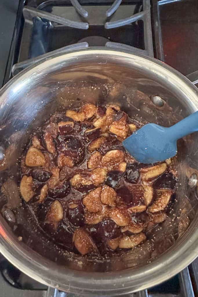 A pan with figs and a blue spatula on top of it.