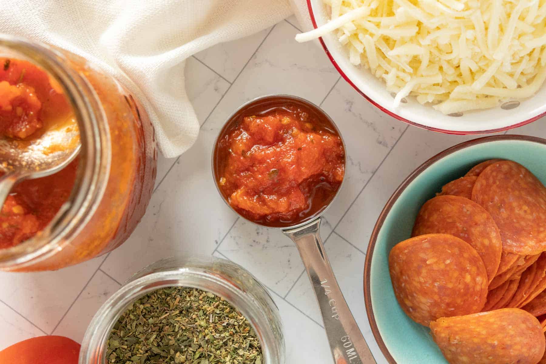 Jars of tomato sauce, pepperoni, cheese and other ingredients on a table.