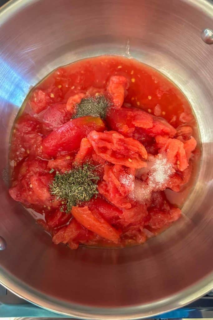 A pot filled with tomatoes and herbs on a stove.